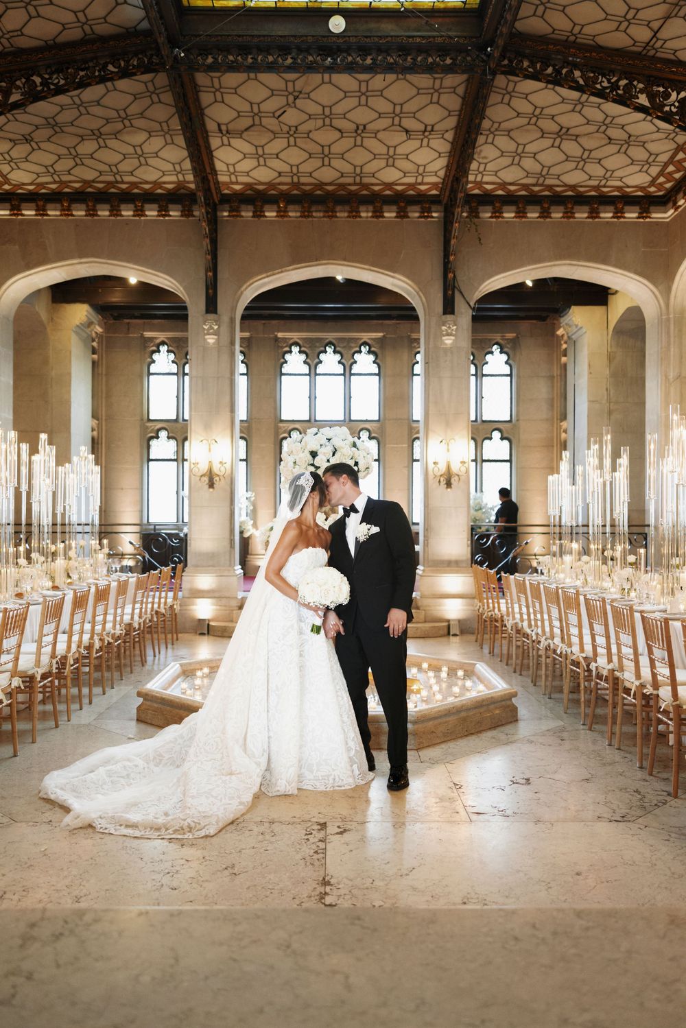 Bride and groom share intimate moment in grand ornate ballroom adorned with candles and florals.