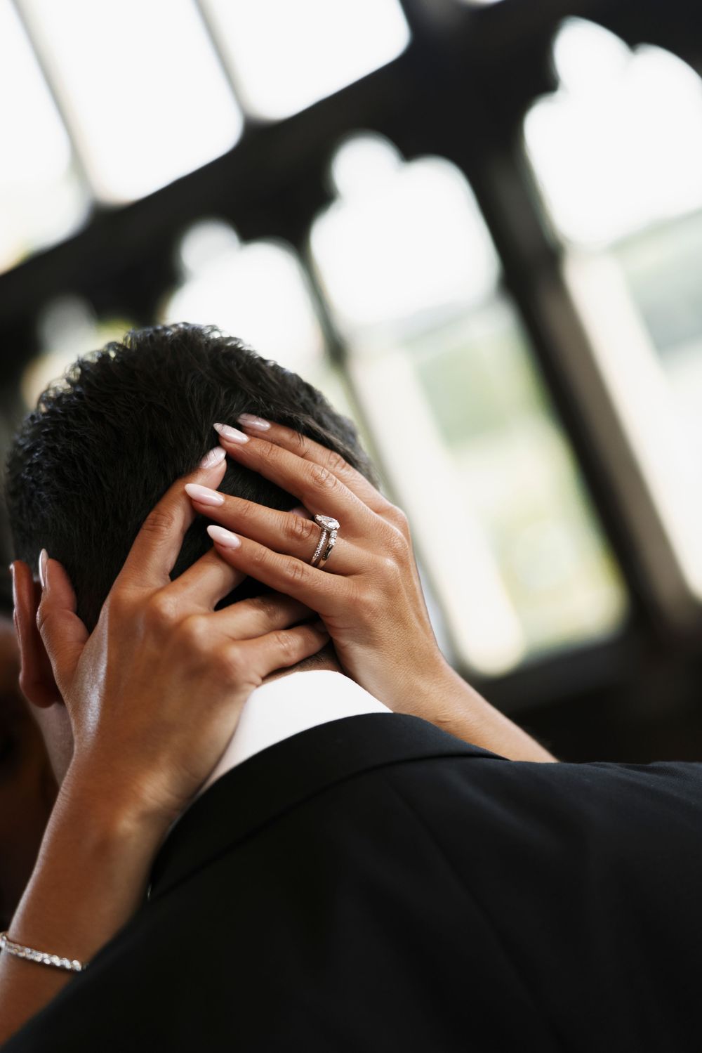 Close-up of bride's hand with diamond ring gently cradling groom's head during intimate moment.