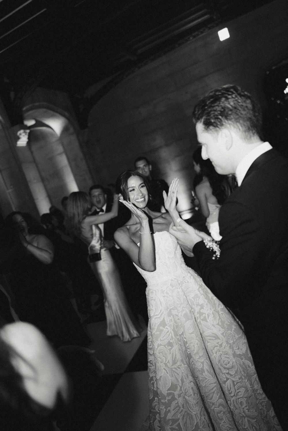 Black and white photo of smiling bride dancing with groom during lively wedding reception celebration.