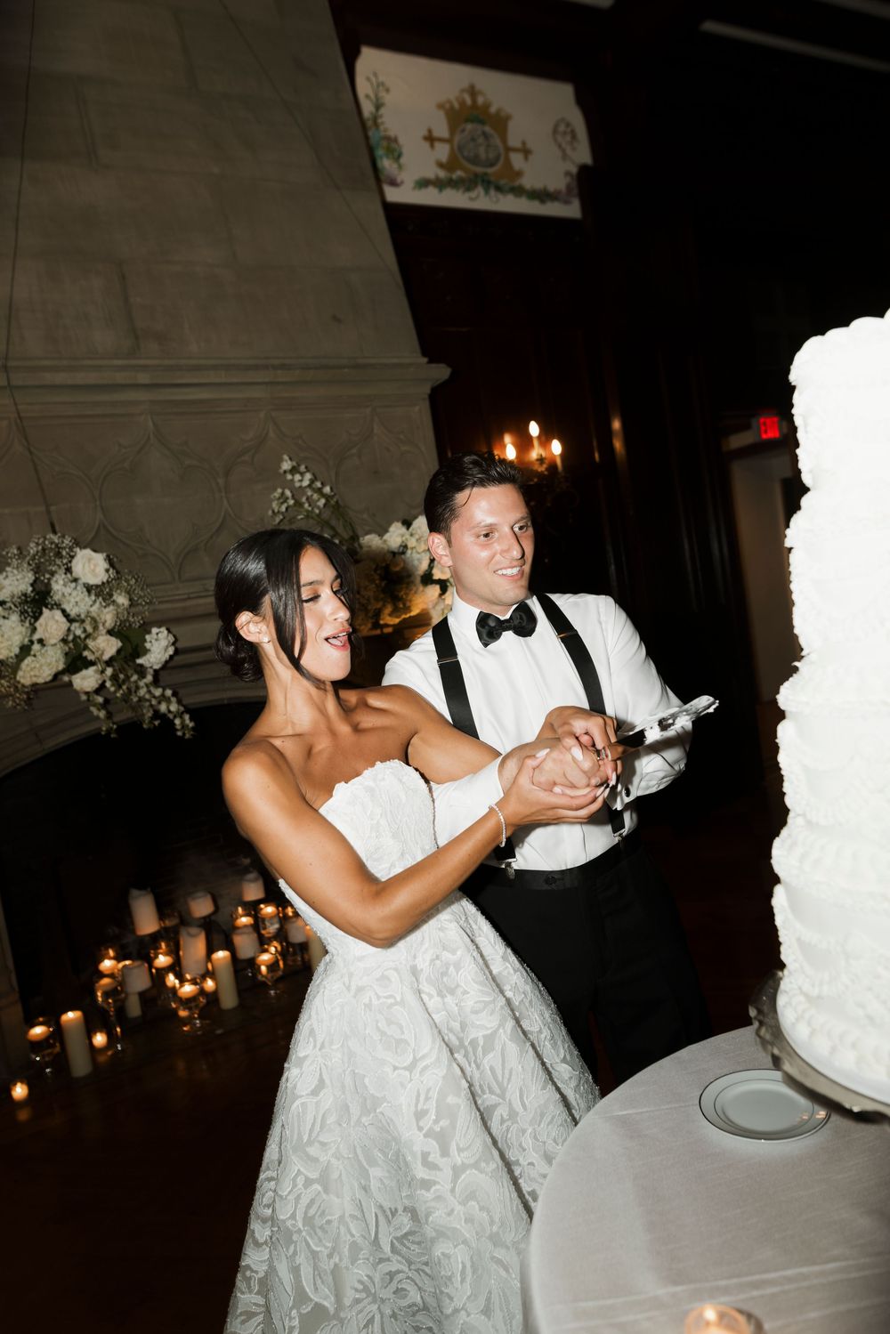 Bride and groom smiling while cutting their white tiered wedding cake surrounded by candles.