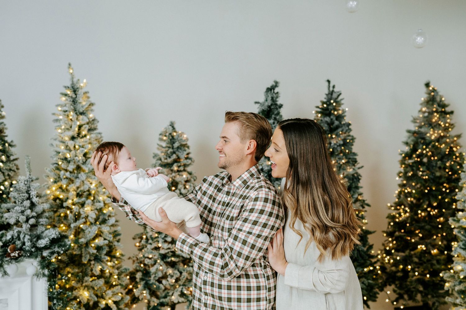 Festive holiday scene with decorated Christmas trees glowing with warm lights against a gray wall.