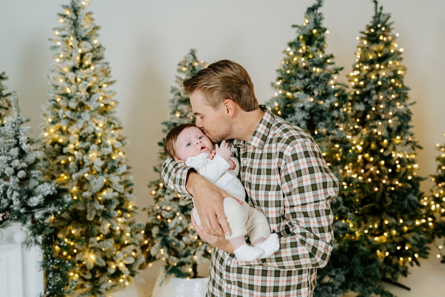 A couple shares romantic holiday moments in front of decorated Christmas trees with twinkling lights.