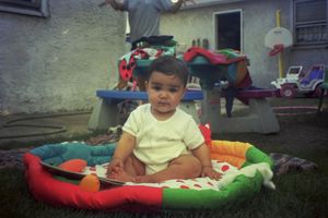 A baby rests on colorful cushions and blankets in a casual indoor setting.