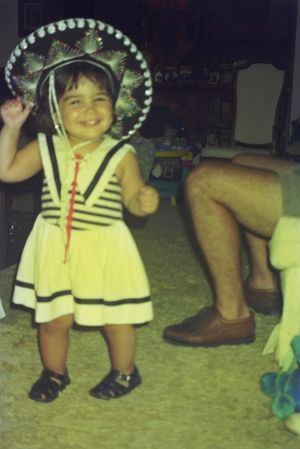 Small child wearing a striped outfit and decorative hat on carpet.
