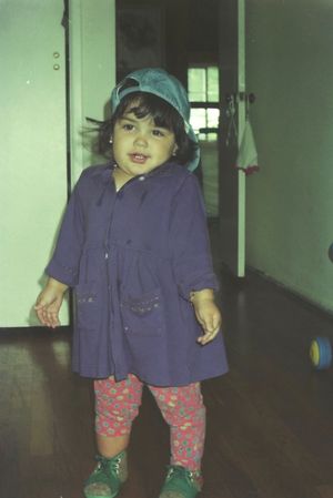 Small child in blue jacket and floral pants standing in hallway.