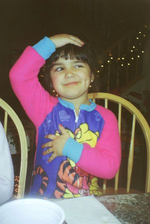 A young child in colorful clothing with a Tigger design poses at a dining table.