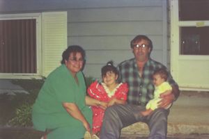 Family members sitting together on steps outside a house with yellow siding.