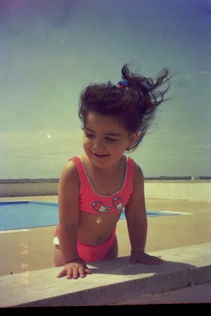Child in pink swimwear leans over a wall at the beach.