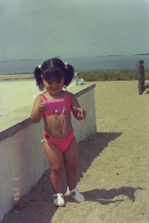 Young child in a pink swimsuit plays on a sunny beach.