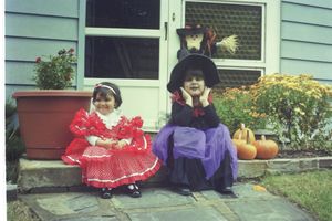 Children sitting on steps outside a blue house with pumpkins nearby.
