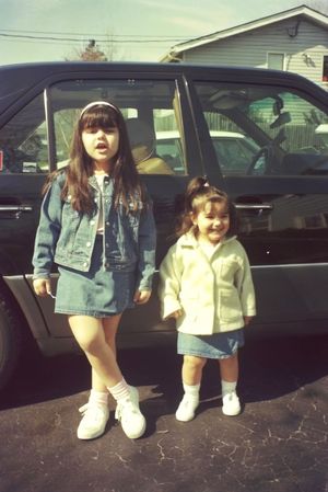 Children standing in matching outfits next to parked cars.