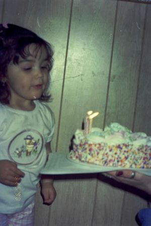 Child holding a birthday cake with lit candles against a white wall.
