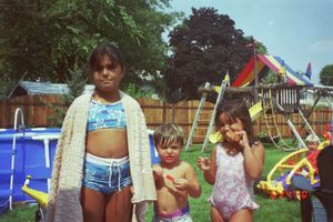 Children playing outdoors in a backyard with playground equipment and toys on a sunny summer day.