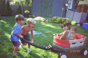 Kids enjoying outdoor playtime with various toys and equipment in a fenced backyard.