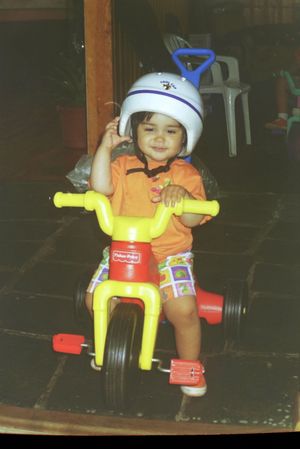Toy tricycle with safety helmet on dark wooden floor.