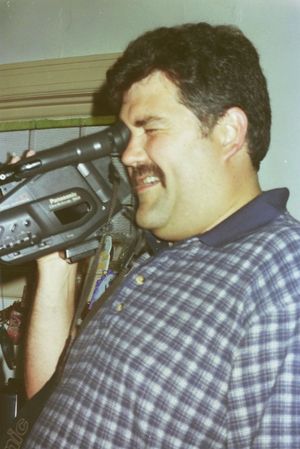 Person using a camcorder while wearing a plaid shirt.