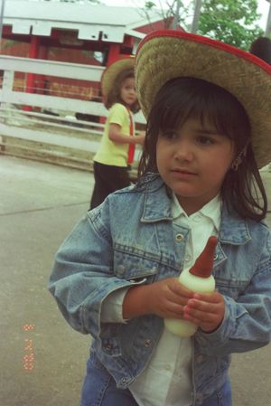 Child wearing denim jacket and straw hat outdoors.