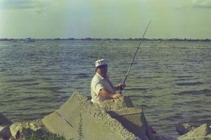 People fishing along the shoreline at sunset with fishing poles.