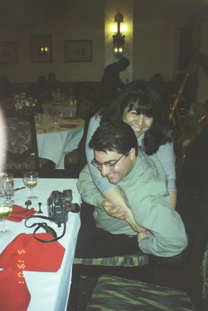 Person in light colored clothing seated at a dining table with red tablecloth.
