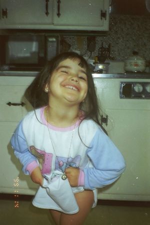 Child wearing blue and white clothing playing and smiling in a kitchen.