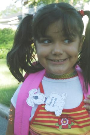 Young child wearing a pink backpack and striped shirt with cartoon character bib.