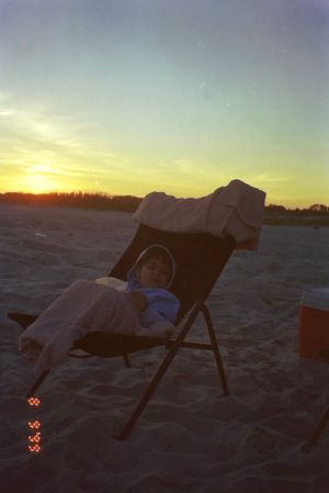 A beach chair silhouetted against a golden sunset over the sand.