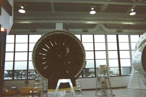 Large jet engine on display in a museum with industrial windows.