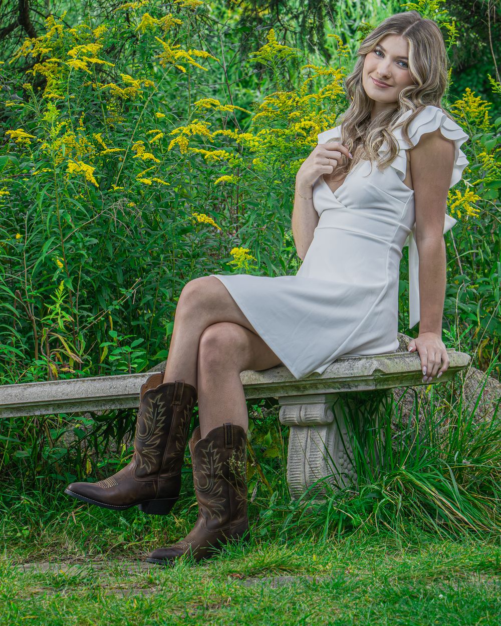 Rustic outdoor portrait session on stone bench surrounded by yellow wildflowers.