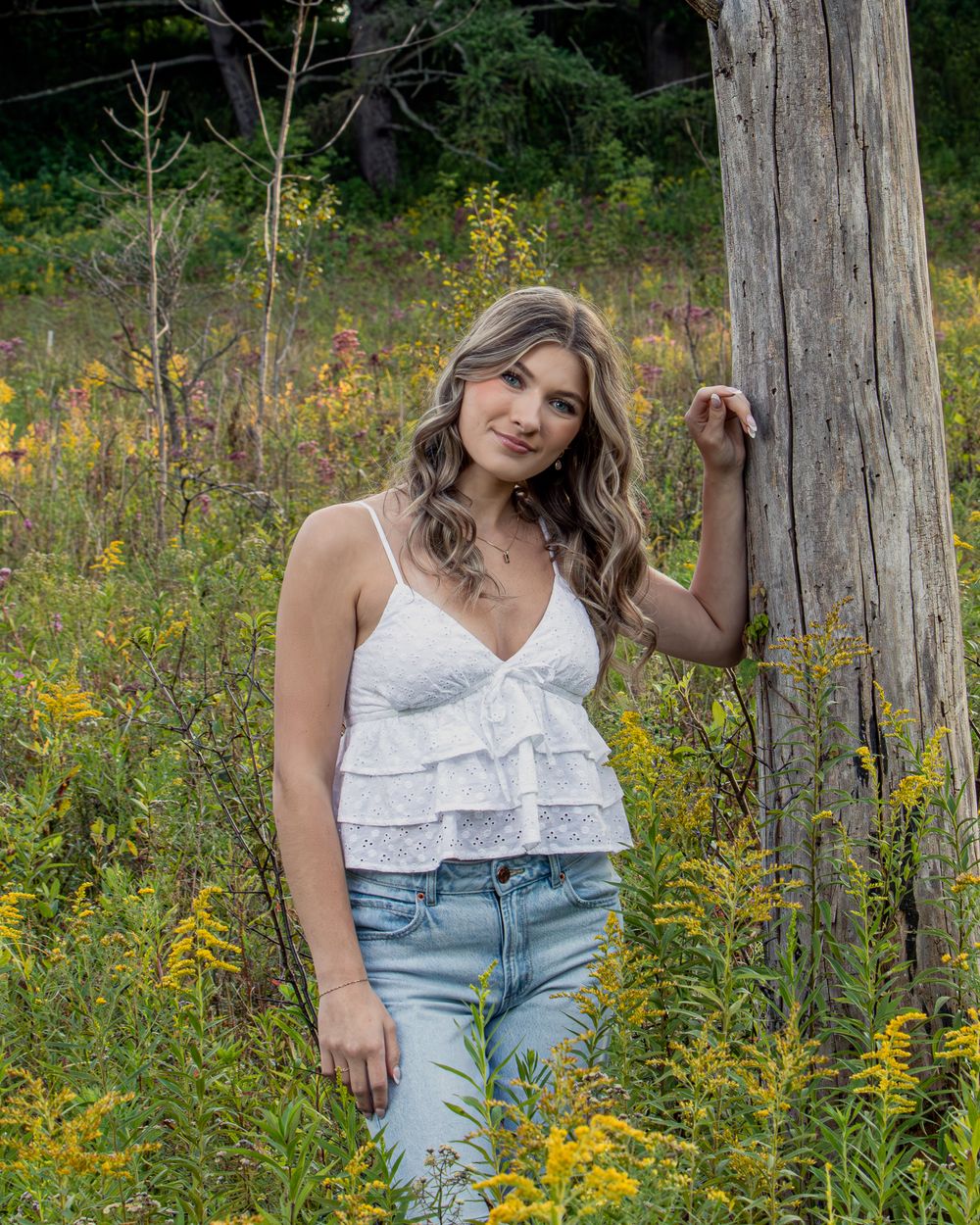 Summer fashion shoot in field with white top and denim against wooden fence.