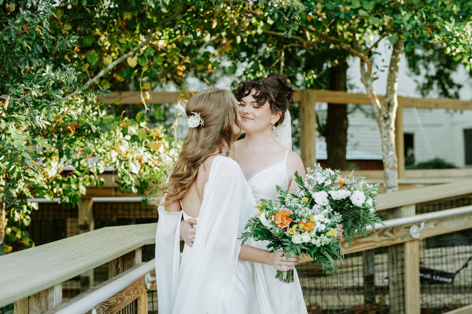 A couple shares a romantic kiss under a rustic wooden pergola decorated with greenery and flowers at an outdoor wedding.