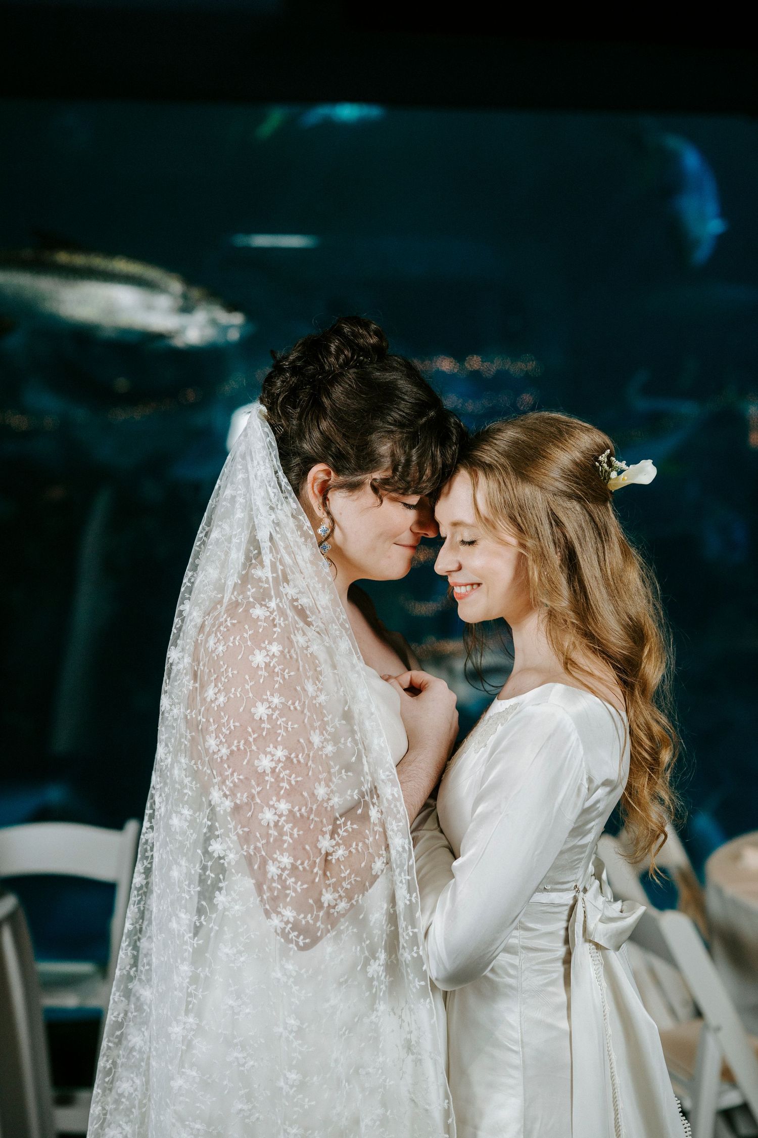 Intimate moment between couple in white captured against dark background with delicate lace veil.