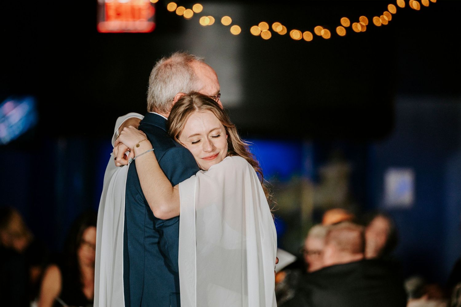 A romantic dance scene at a wedding reception with soft lighting and string lights overhead.