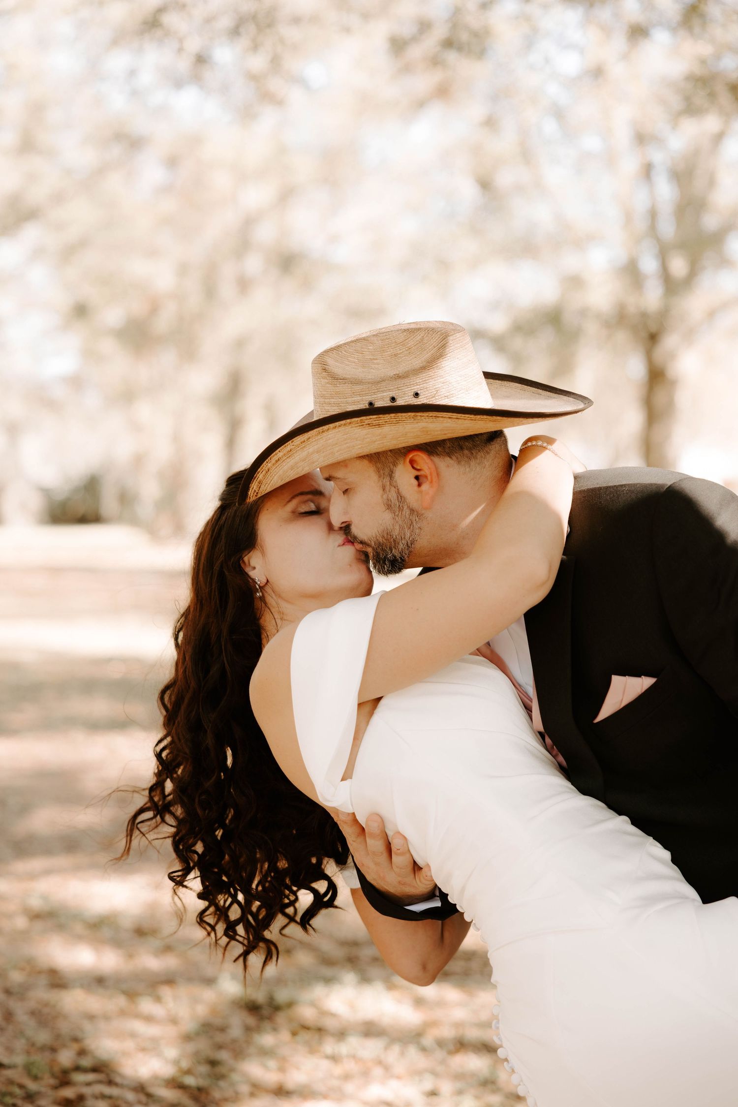 A romantic wedding couple shares intimate kisses in a dreamy outdoor setting with soft sepia tones.