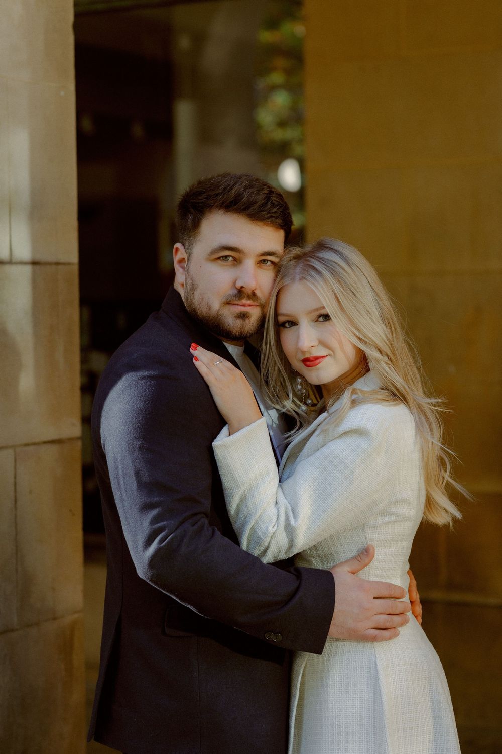 A romantic couple embraces in a series of intimate poses against a warm-toned architectural backdrop.