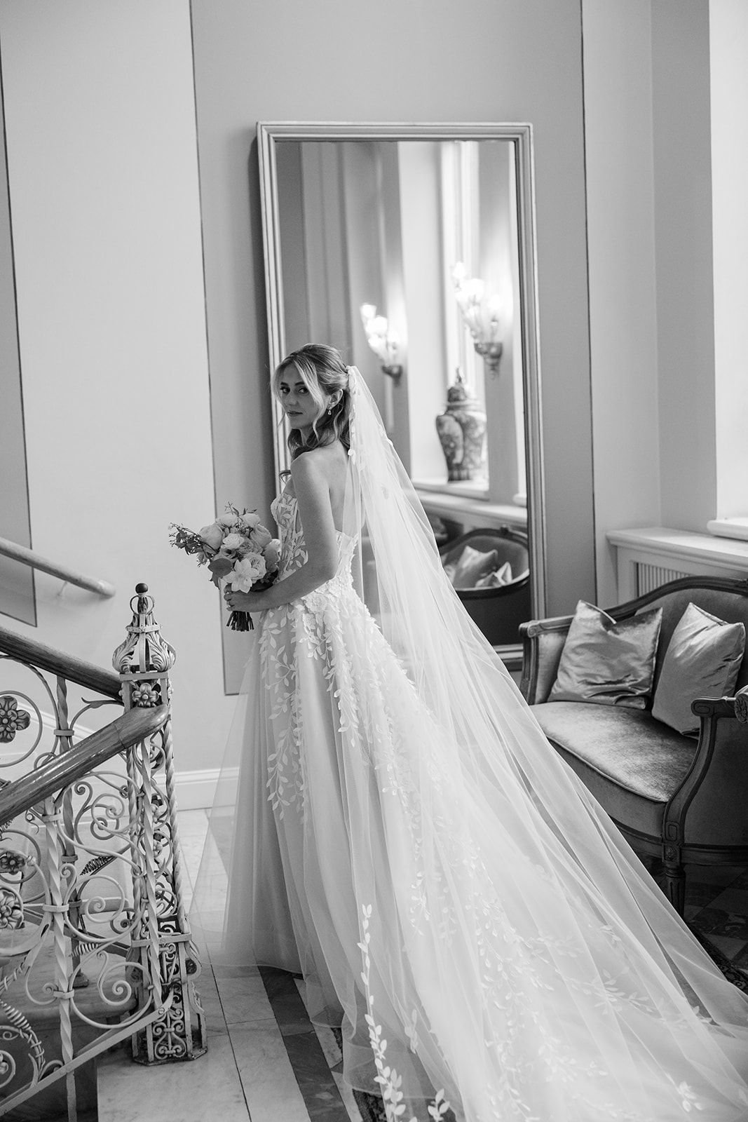 Black and white photograph of wedding dresses with delicate floral embellishments hanging in a bridal shop window.
