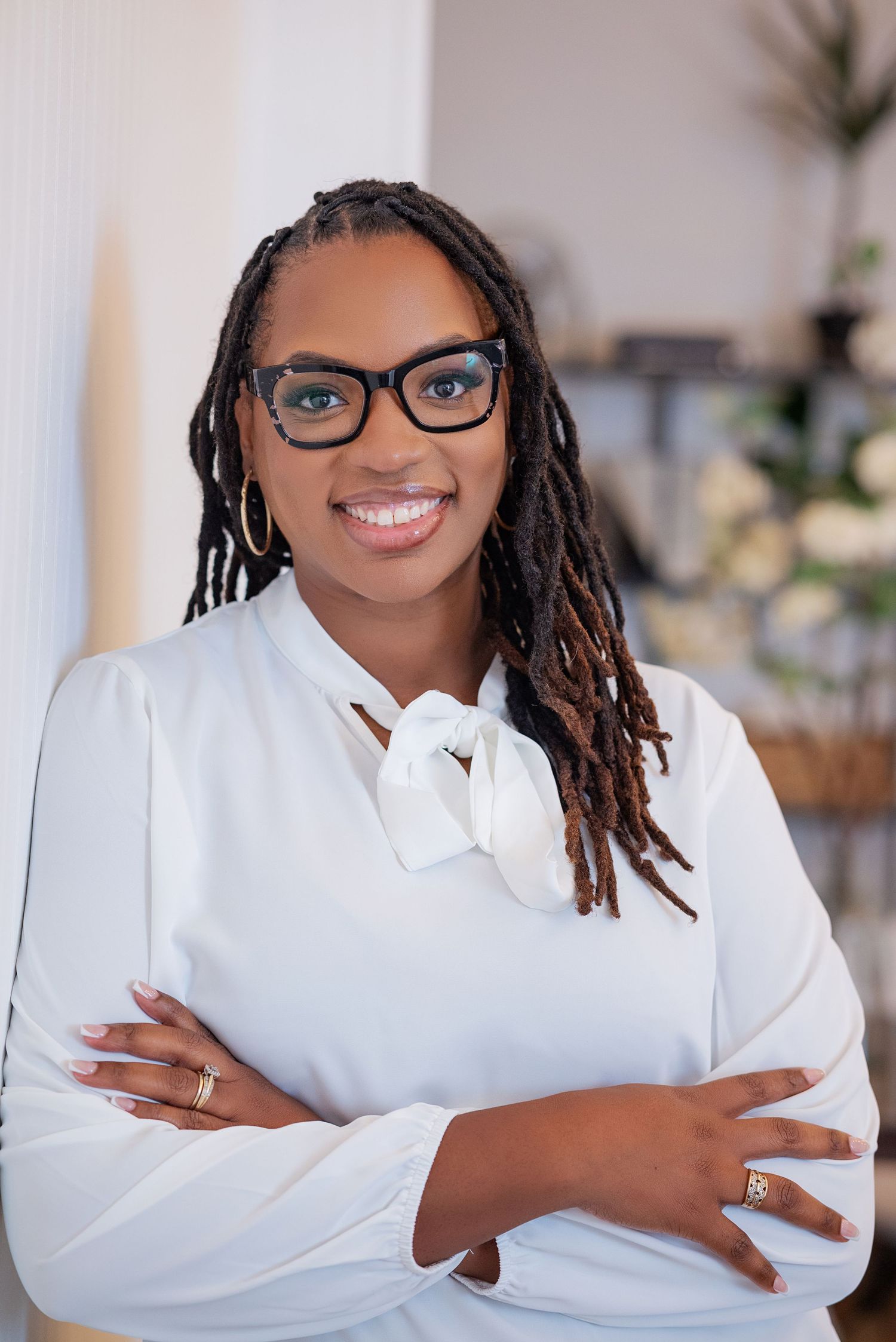 Professional headshot of someone in a white button-down shirt and glasses smiling warmly at the camera.