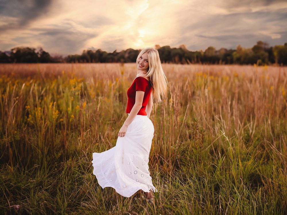 A senior girl in a flowing white dress walks through a golden wheat field at sunset. Maxwell Studios Best Senior photographer in Central IL.