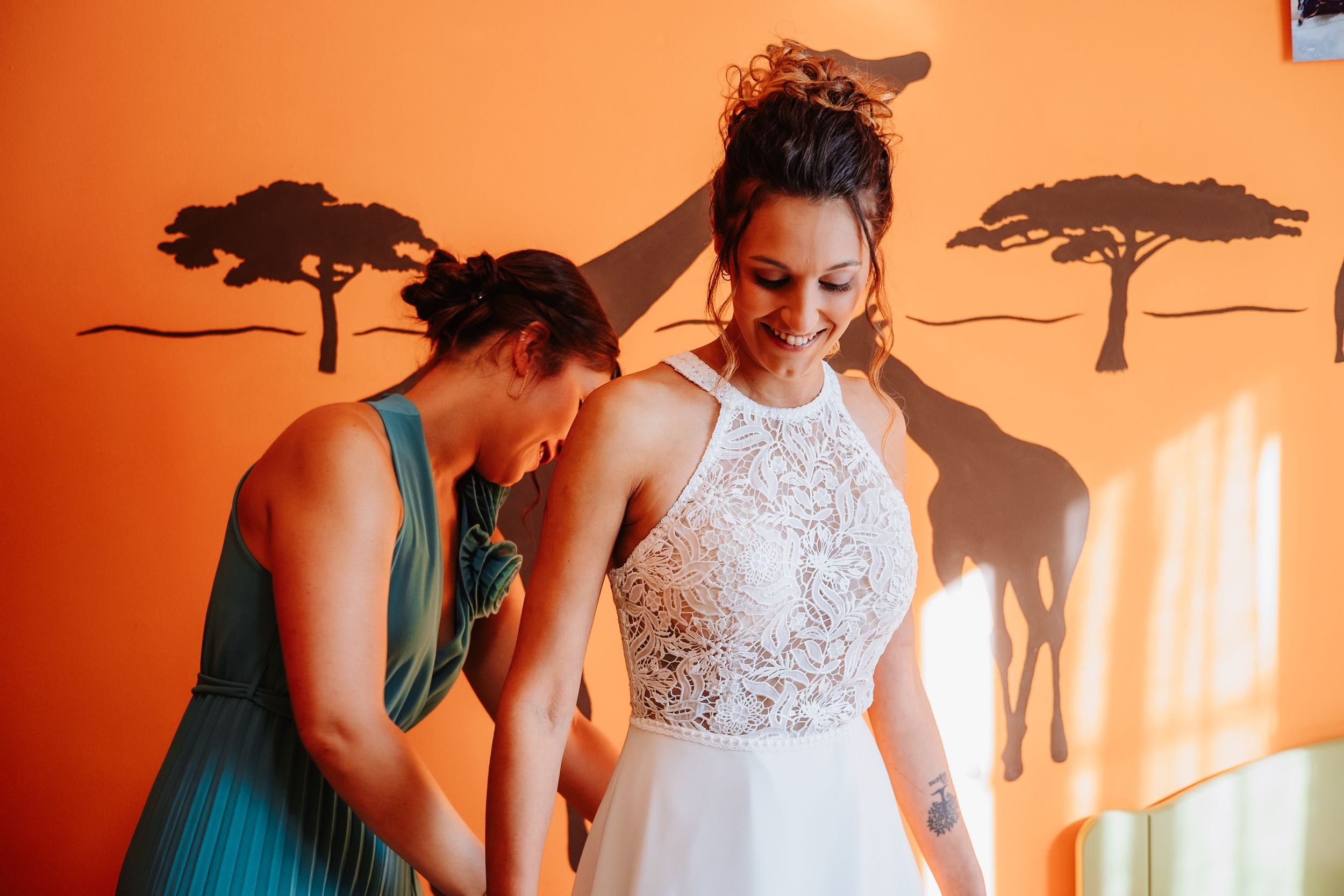 A wedding party in teal dresses and white gown gathers together in a warm sunlit room.