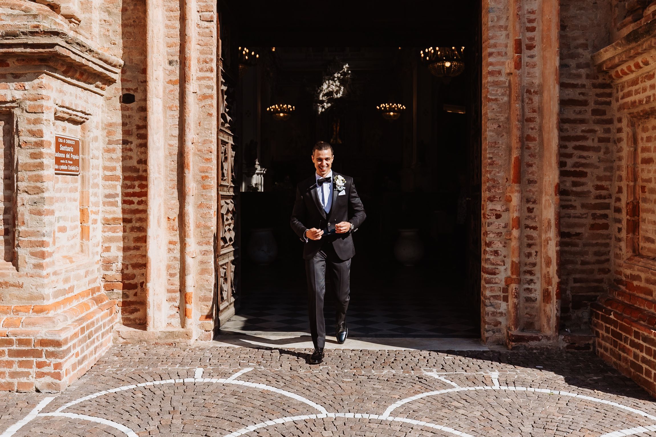 A couple in formal wedding attire stands in an arched brick doorway of a historic building.
