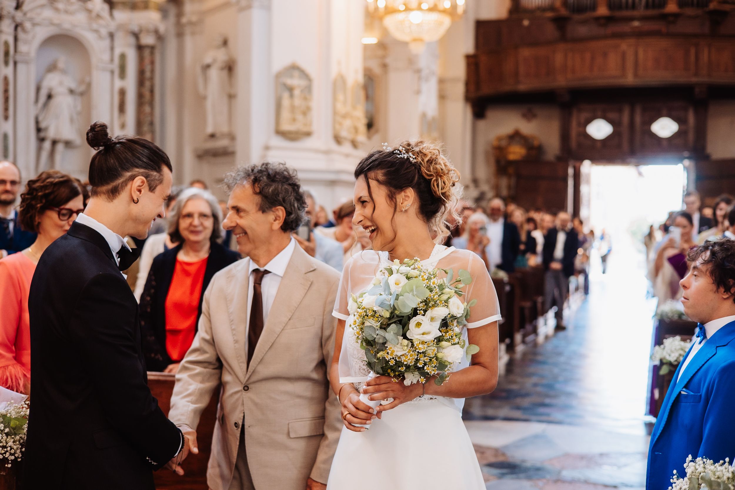 Couple exchanging rings during traditional wedding ceremony in an ornate church with elegant chandeliers.