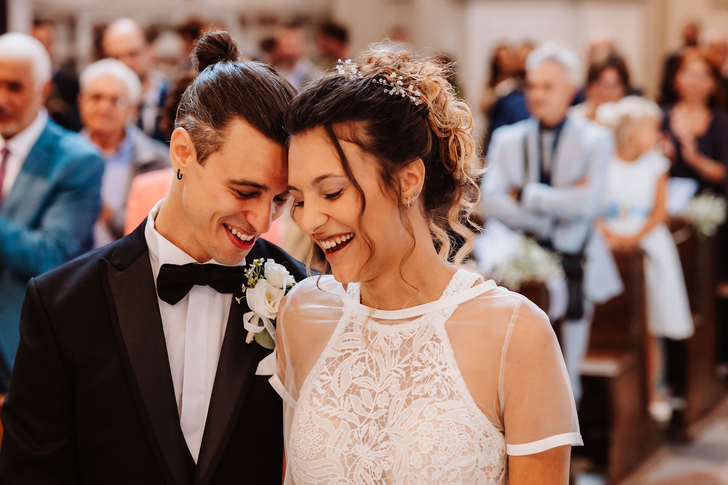 A joyful wedding moment captured as newlyweds share a laugh during their ceremony with guests in the background.
