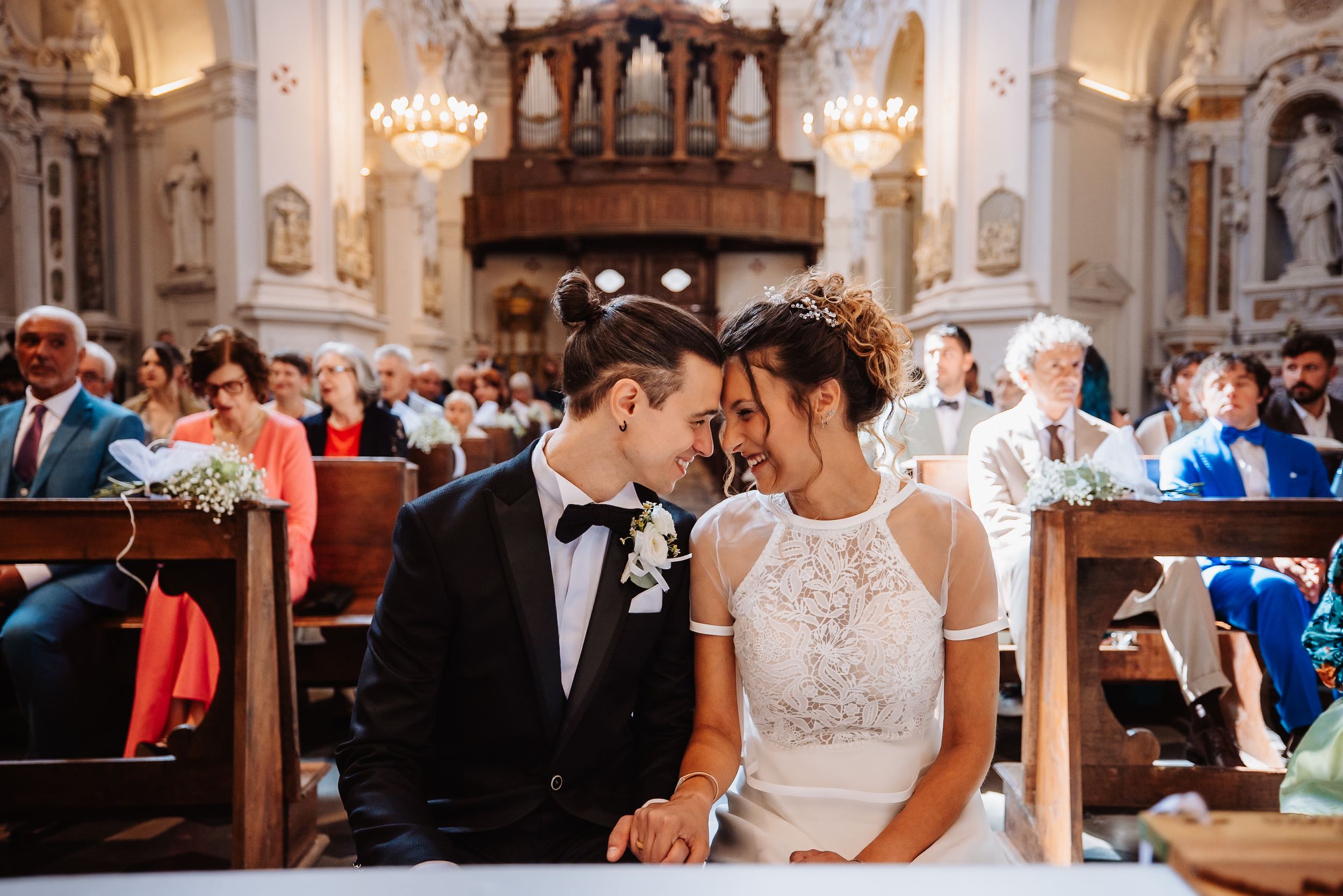 Couple shares a romantic moment during their wedding ceremony in an ornate church with elegant architecture and lighting.
