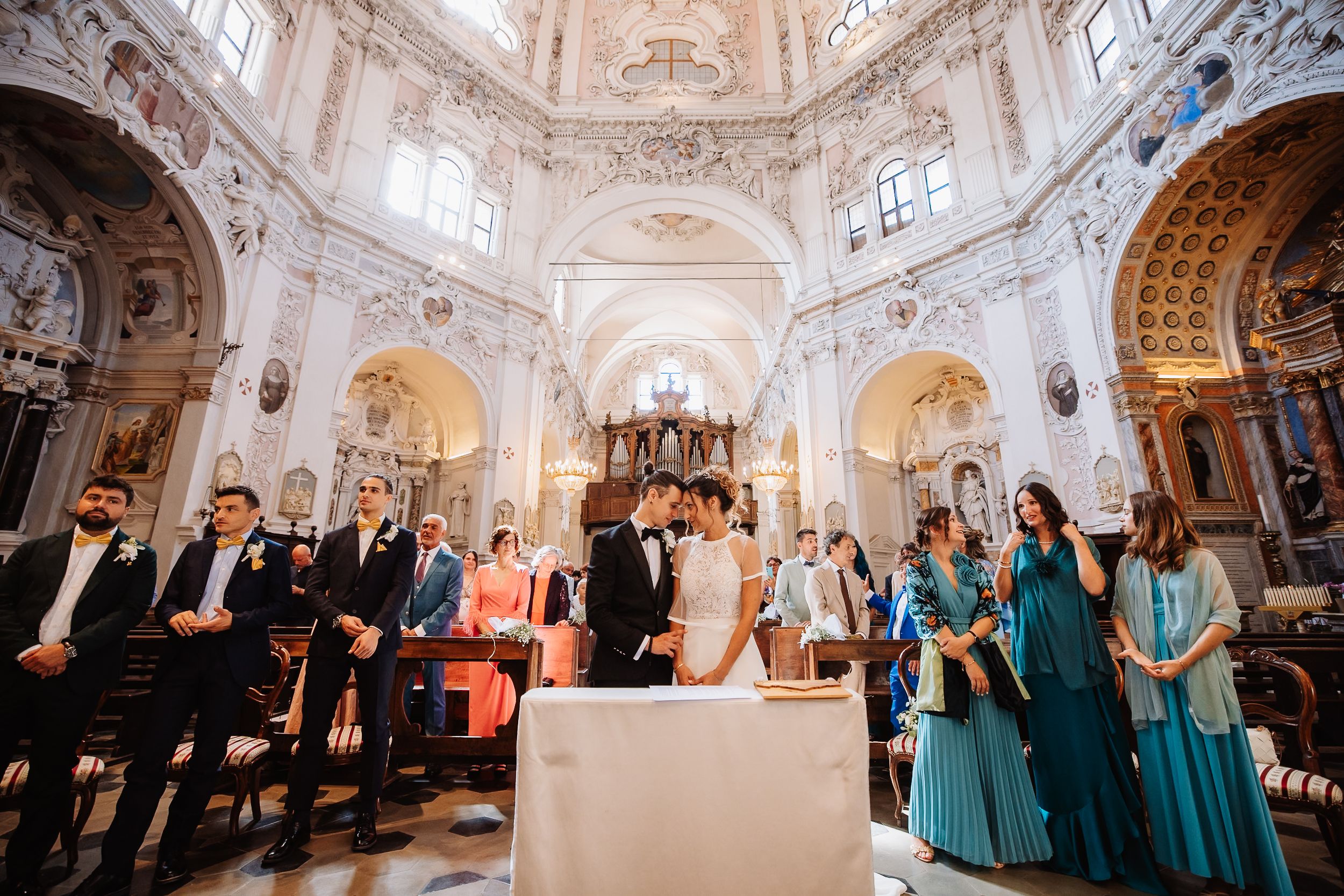 A panoramic view of an ornate church ceremony with guests gathered in formal attire beneath baroque architecture.
