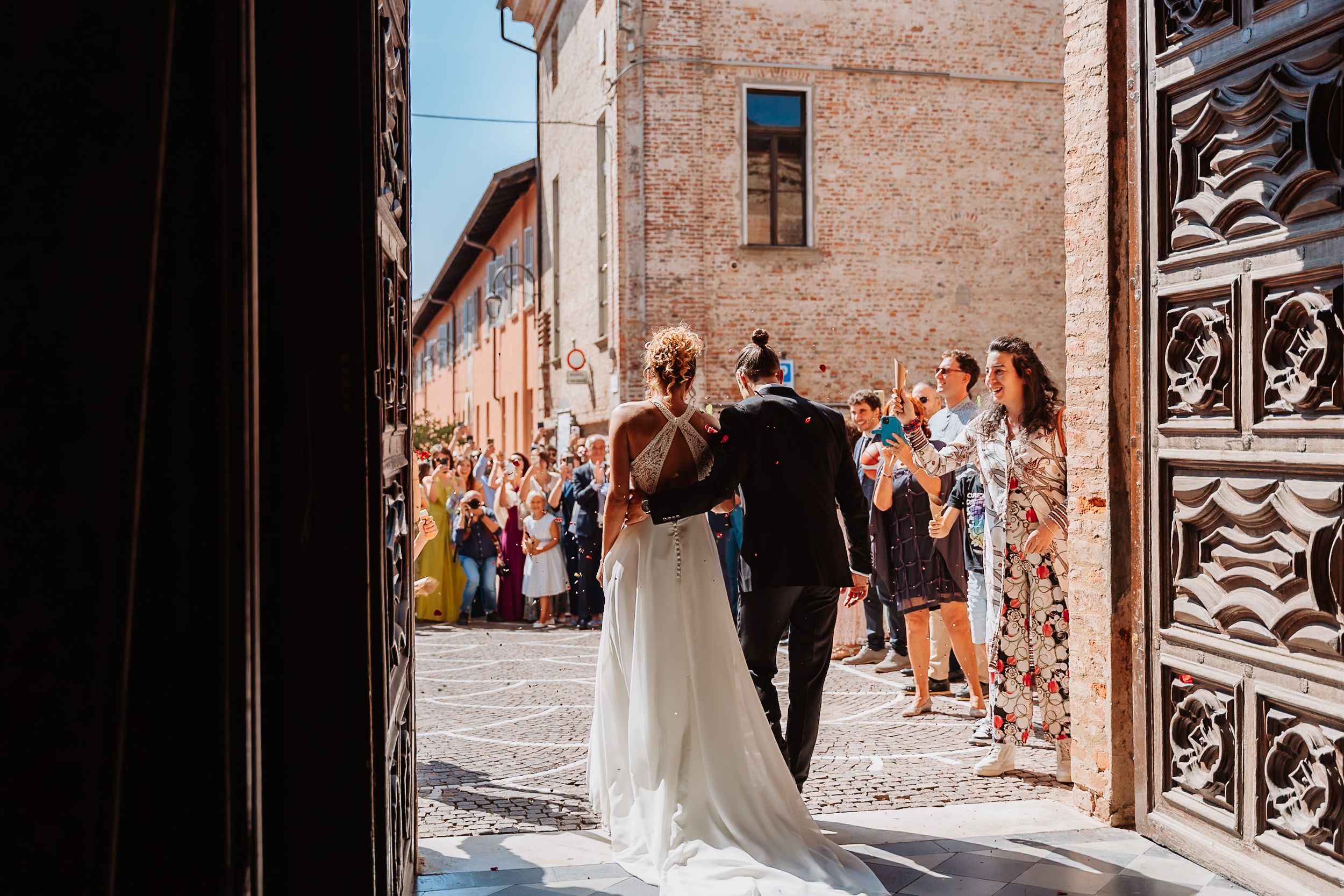 Wedding party walks through historic stone alleyway with rustic brick walls and decorative iron gates.