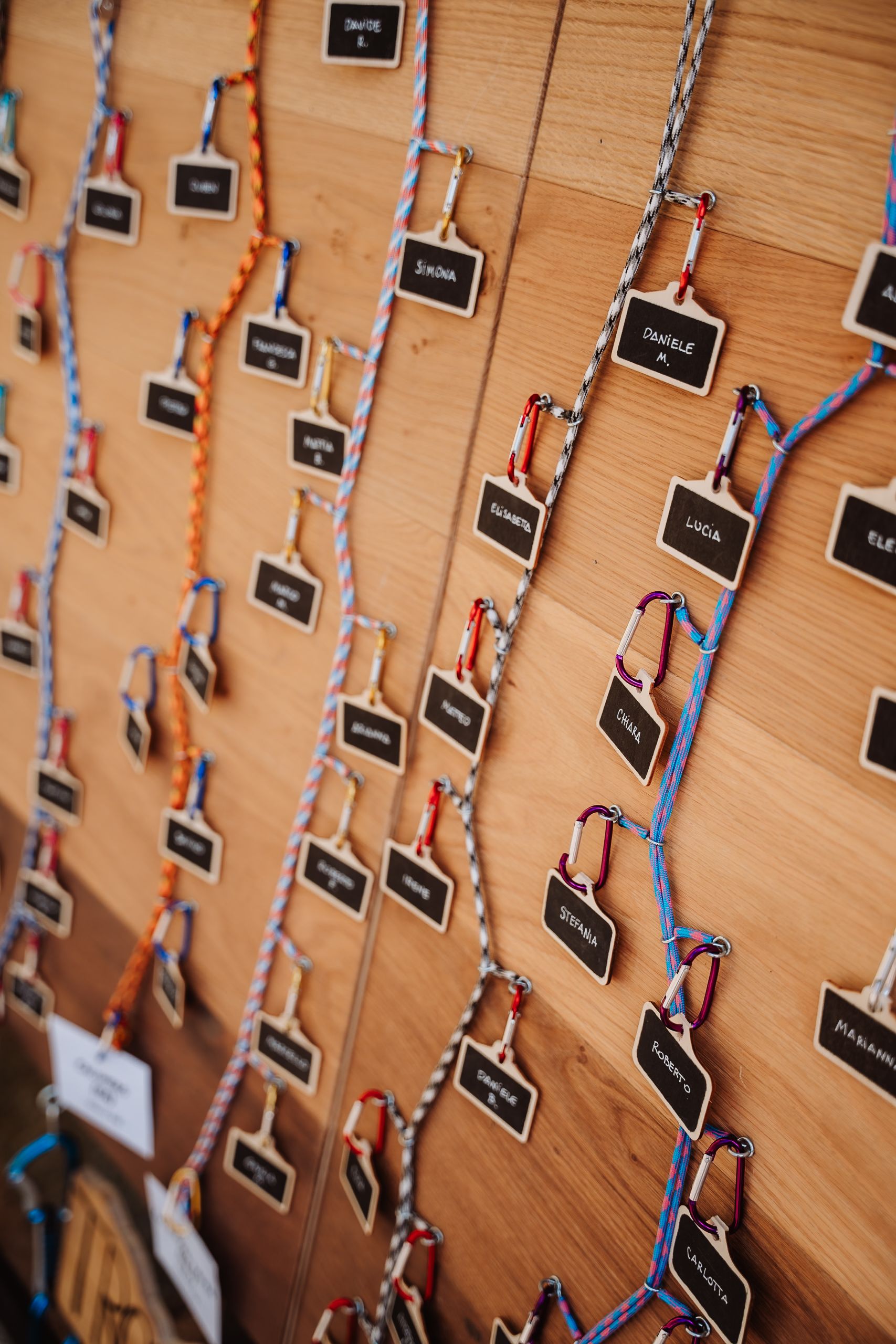 Multiple small chalkboard name tags hanging on colorful strings against a wooden wall create an organized display pattern.
