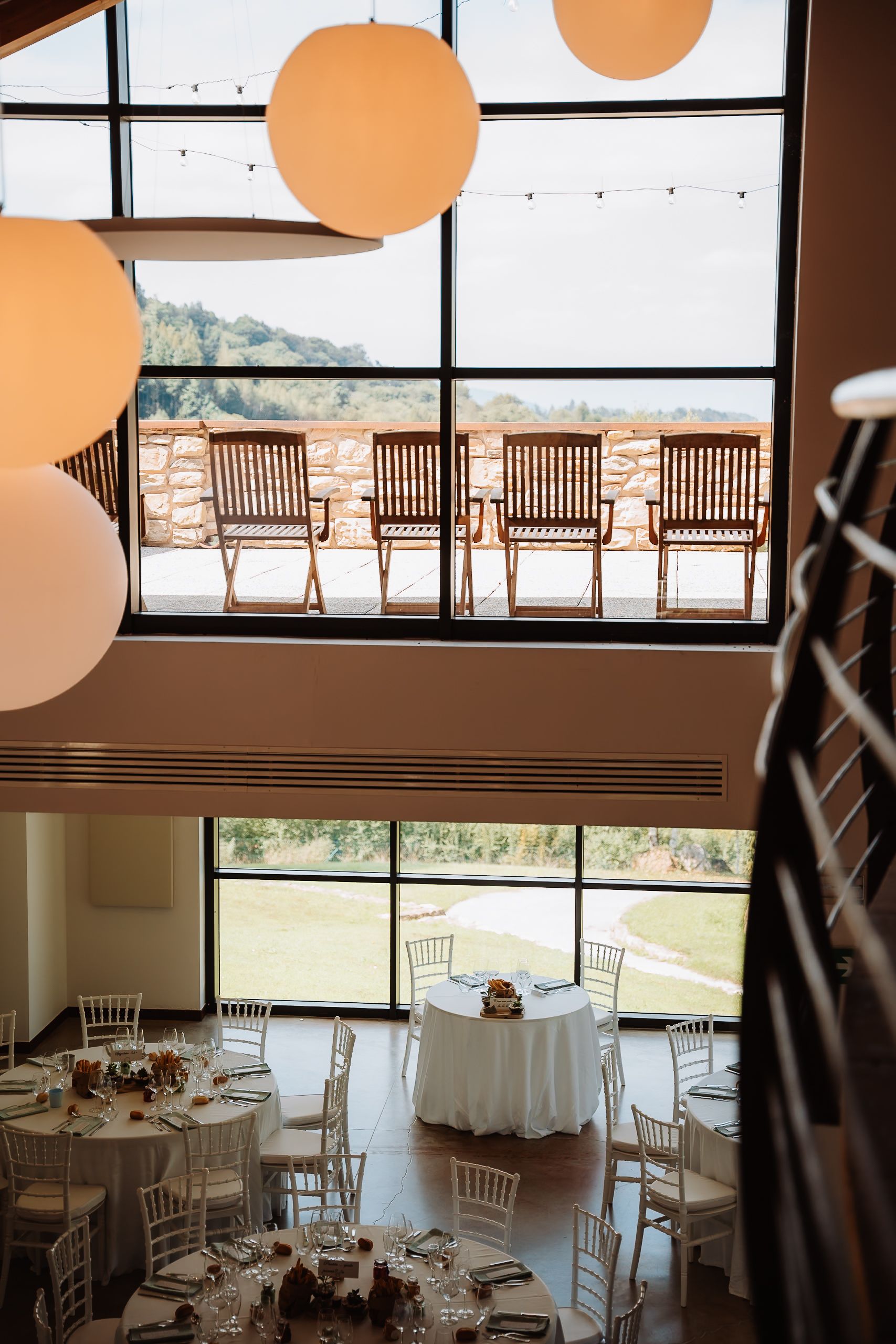 Elegant wedding reception venue with white tables, wooden chairs, and large windows overlooking scenic mountain views.