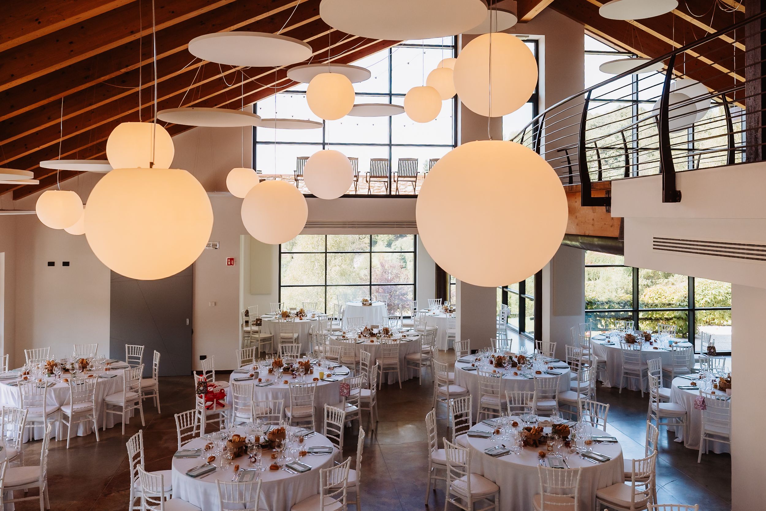 Modern event space with white tables and paper lantern decorations hanging from exposed wooden beams in the ceiling.