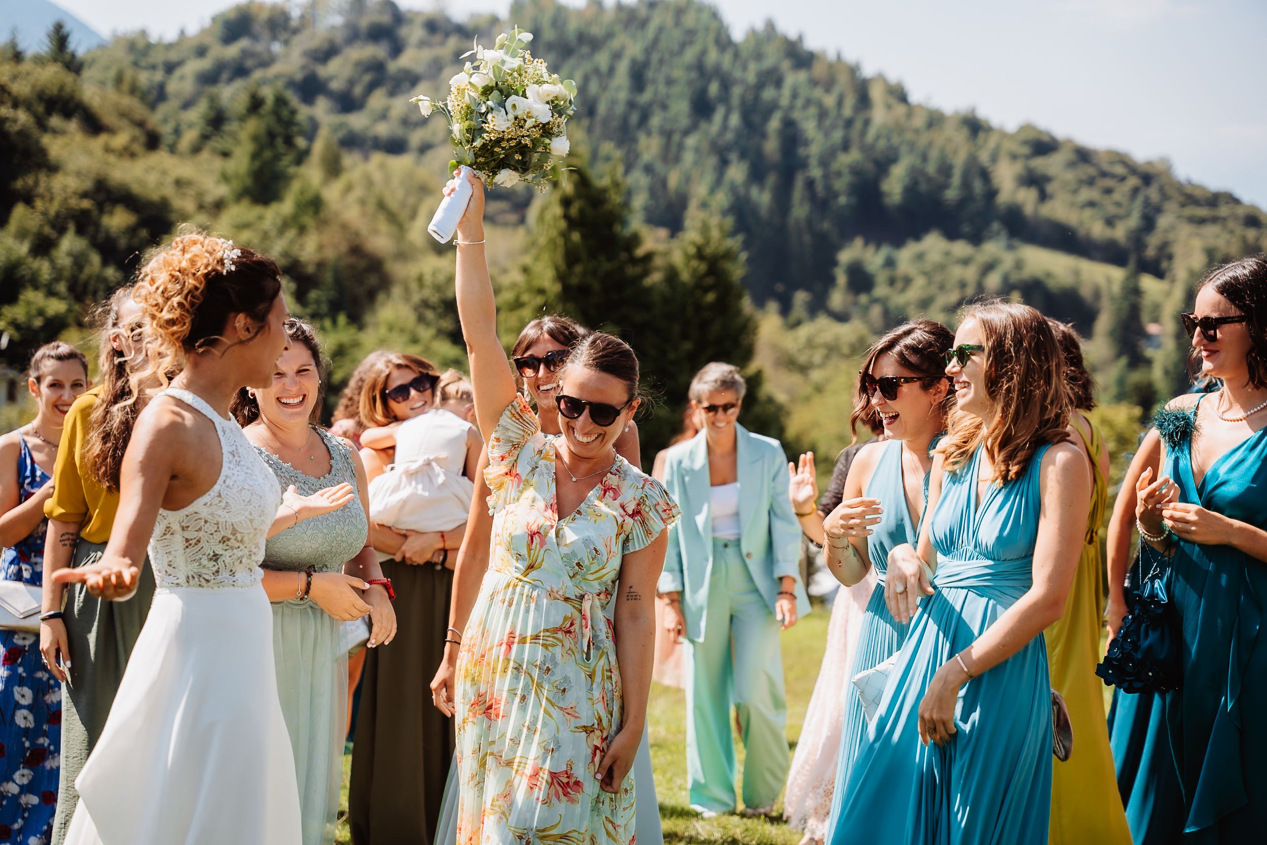 Wedding party in coordinated blue and mint green attire stands together outdoors against mountain backdrop.