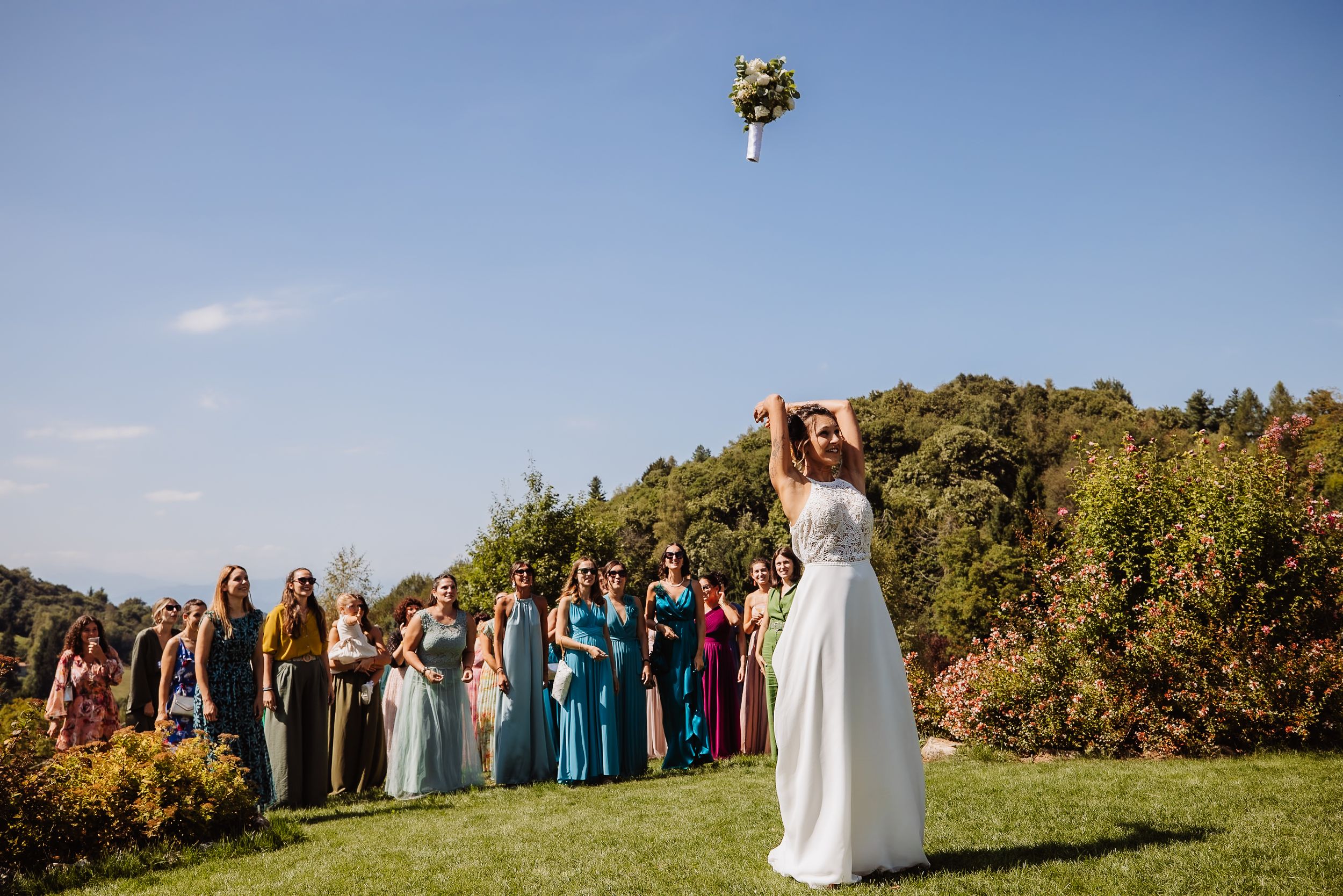 Wedding party standing in a line against a scenic hilltop backdrop with autumn foliage and blue sky.