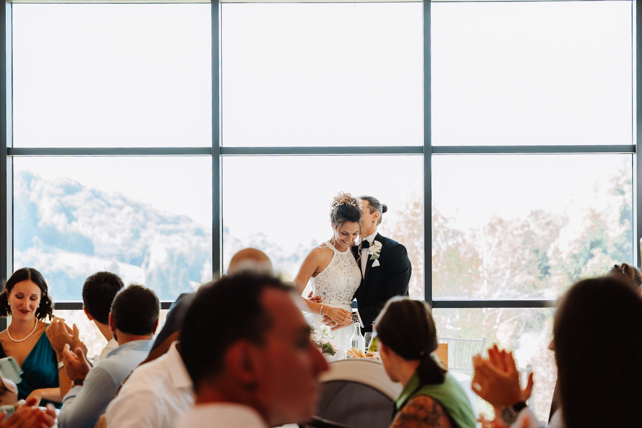 A crowd of people gathered in front of large windows overlooking a scenic mountain landscape.